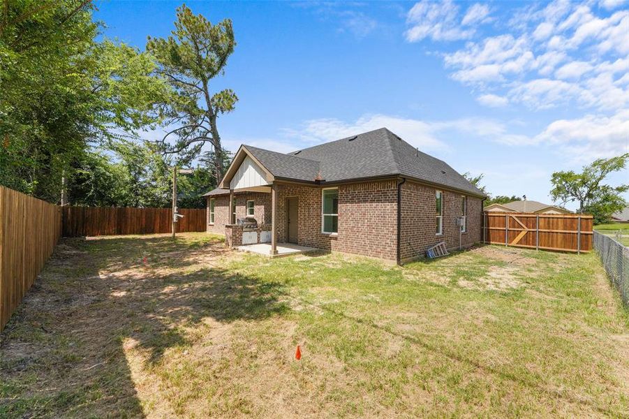 Brick exterior home featuring a covered patio, a built-in outdoor cooking station, a newly installed wood fence, and a chain-link fence