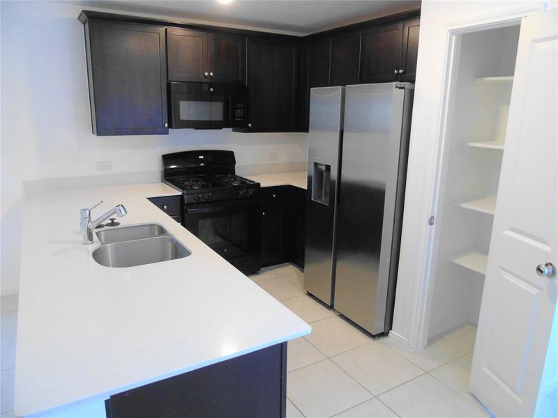 Kitchen with light tile patterned floors, dark brown cabinets, sink, and black appliances