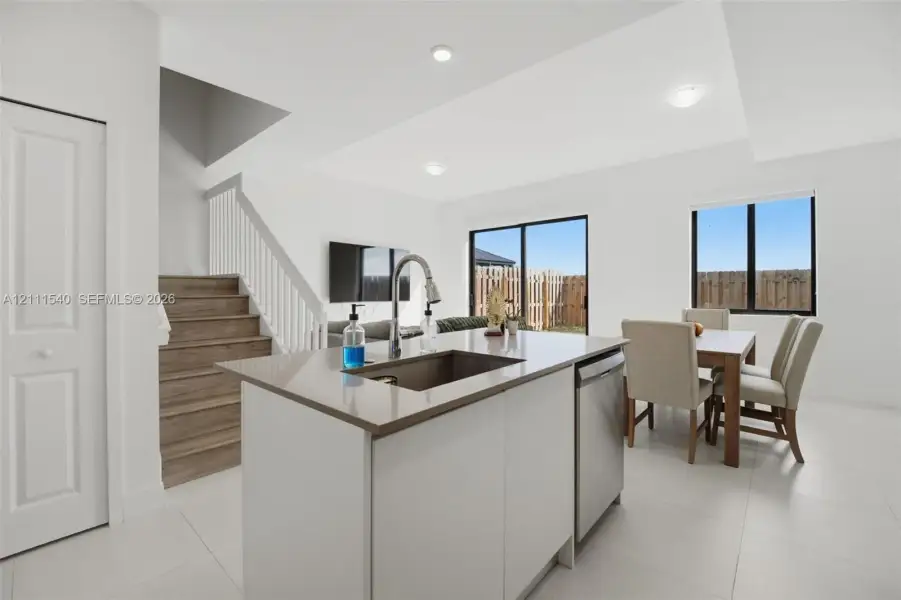Kitchen island with stone-surface countertop, stainless steel undermount sink, wood-finish stairs with white railing, and sliding glass doors