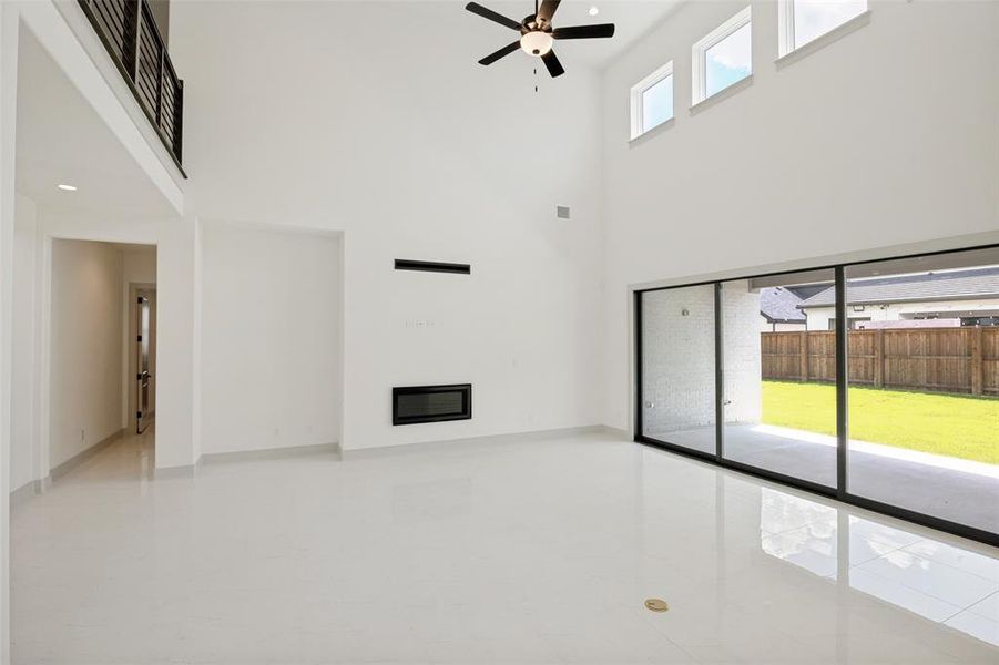 Spacious living area featuring high ceilings, white tile flooring, and a modern fireplace Spacious living area featuring high ceilings, white tile flooring, and a modern fireplace