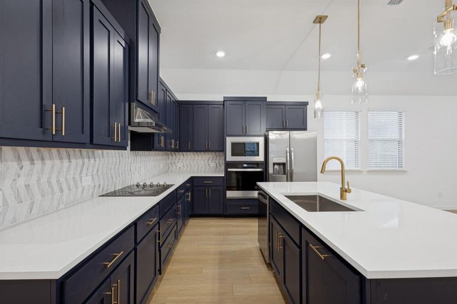 Kitchen featuring dark cabinetry with gold-finish hardware, light countertops, and a chevron-patterned tile backsplash