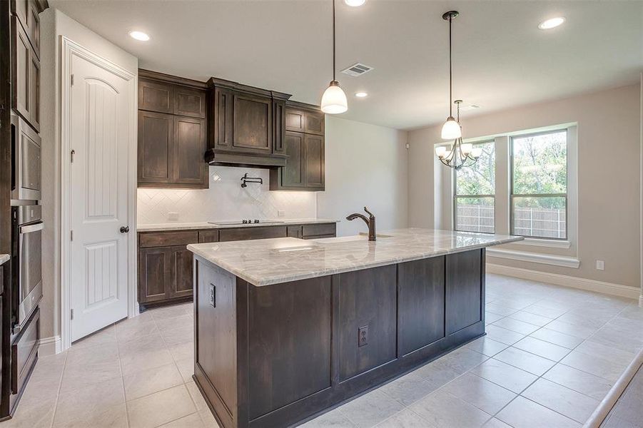 Kitchen featuring dark brown cabinets, a center island with sink, appliances with stainless steel finishes, light stone counters, and tasteful backsplash