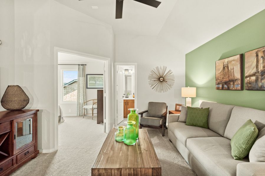 Living room with vaulted ceiling, gray sofa, green accent wall, and ceiling fan, open to bedroom and bathroom