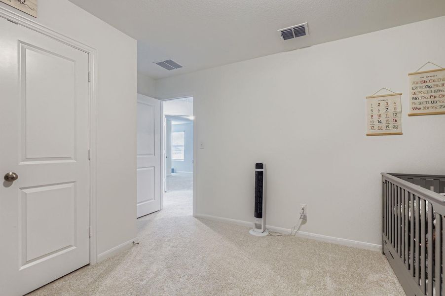 Unfurnished bedroom featuring a nursery area and light colored carpet