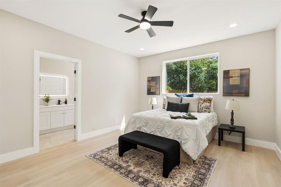 Recessed lighting and a ceiling fan with integrated lighting illuminate this bedroom, featuring light wood-finish flooring and a bright window with exterior tree foliage Recessed lighting and a ceiling fan with integrated lighting illuminate this bedroom, featuring light wood-finish flooring and a bright window with exterior tree foliage