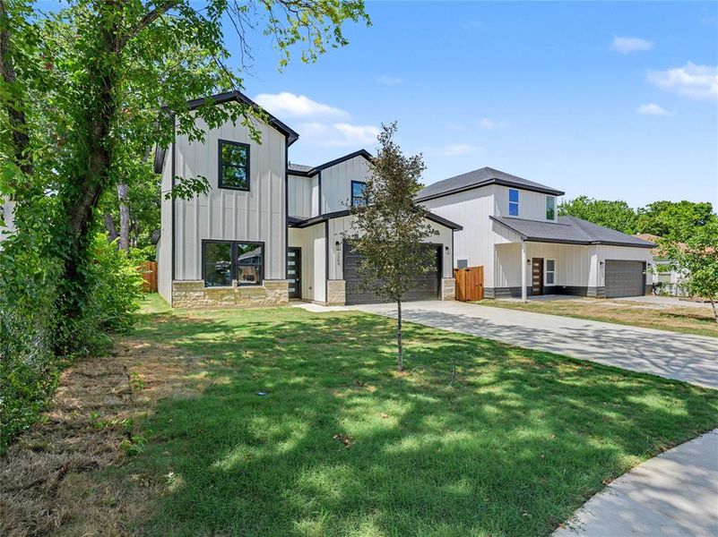 Modern architecture with board and batten siding, stone accents, black window frames, and an attached two-car garage Modern architecture with board and batten siding, stone accents, black window frames, and an attached two-car garage