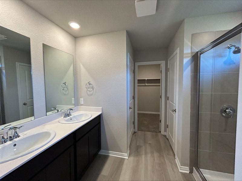 Full bathroom featuring wood finished floors, a stall shower, double vanity, a walk in closet, and a textured wall Full bathroom featuring wood finished floors, a stall shower, double vanity, a walk in closet, and a textured wall