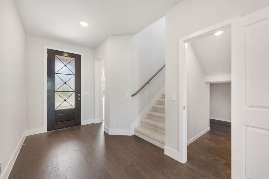 Entryway with dark wood front door, glass panels, hardwood floors, and carpeted staircase nearby. Entryway with dark wood front door, glass panels, hardwood floors, and carpeted staircase nearby.