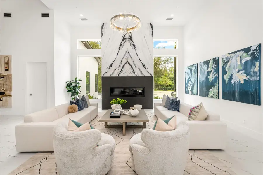 A striking black and white matchbook porcelain feature wall creates a bold focal point above the sleek linear electric fireplace in the formal living room. The space is further enhanced by a pair of circular crystal and matte gold chandeliers, adding a refined touch of modern luxury A striking black and white matchbook porcelain feature wall creates a bold focal point above the sleek linear electric fireplace in the formal living room. The space is further enhanced by a pair of circular crystal and matte gold chandeliers, adding a refined touch of modern luxury