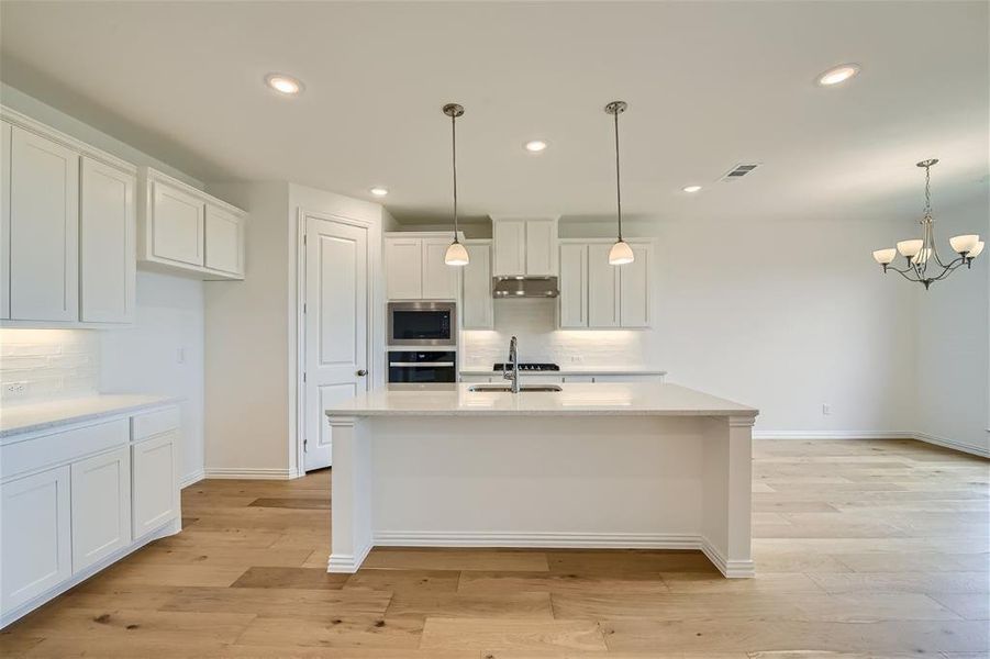 Kitchen with hanging light fixtures, backsplash, and light hardwood / wood-style flooring