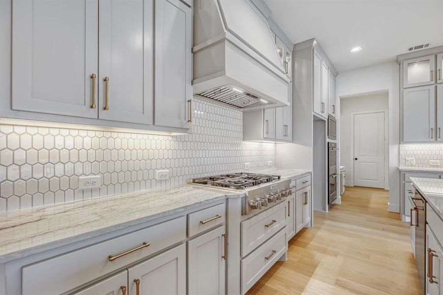Kitchen featuring light stone counters, light wood-style floors, glass insert cabinets, stainless steel appliances, and recessed lighting