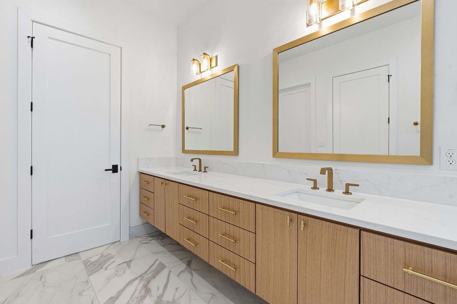 Gleaming flooring underscores a handsome double vanity equipped with gold-toned fixtures and matching mirrors.