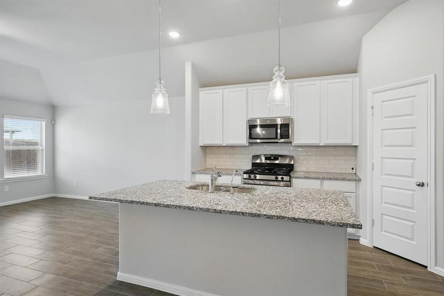 Kitchen with appliances with stainless steel finishes, vaulted ceiling, tasteful backsplash, dark wood-style flooring, and white cabinetry Kitchen with appliances with stainless steel finishes, vaulted ceiling, tasteful backsplash, dark wood-style flooring, and white cabinetry