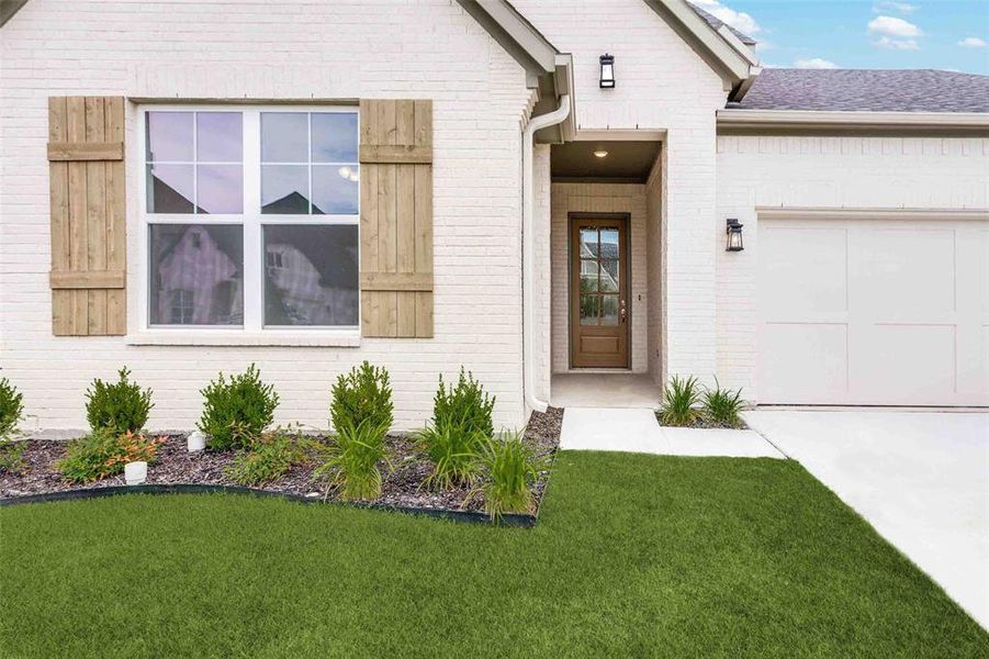 Property entrance with brick siding, a garage, a lawn, concrete driveway, and roof with shingles