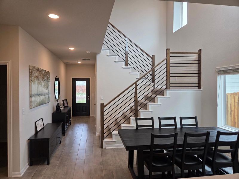 Two-story foyer featuring a wood-finish tile flooring, a modern staircase with dark wood newel posts and horizontal metal balusters, recessed lighting, and a front entry door with decorative glass inserts
