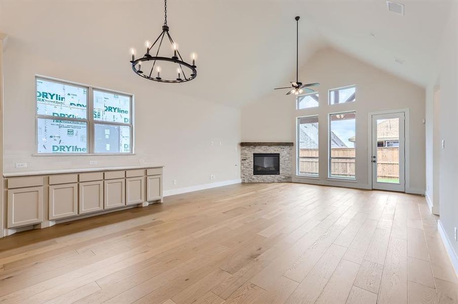 Unfurnished living room with ceiling fan with notable chandelier, a stone fireplace, light hardwood / wood-style flooring, and high vaulted ceiling