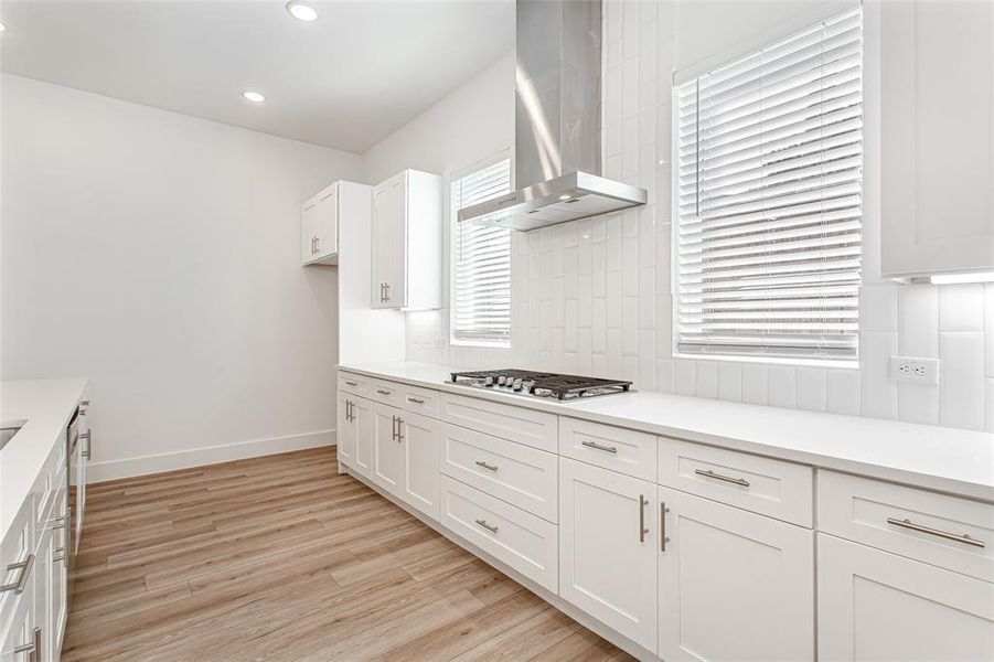 Kitchen featuring white cabinets, exhaust hood, light wood-type flooring, recessed lighting, and tasteful backsplash