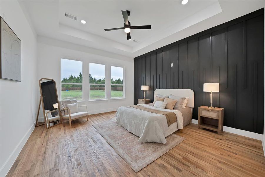 Well-appointed room featuring hardwood flooring, a contrasting accent wall with vertical paneling, and a tray ceiling