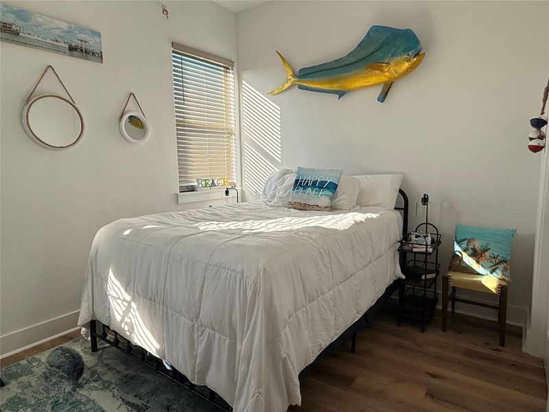 Bright and cozy bedroom with a nautical theme, featuring a double bed, coastal decor, and abundant natural light from a window with blinds.