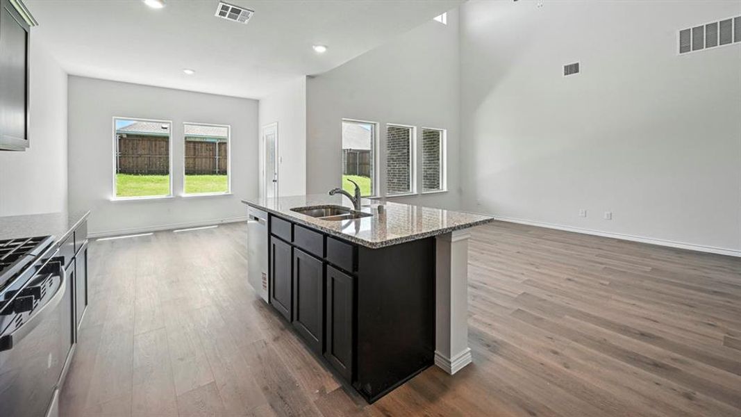 Open-concept living area featuring a kitchen island with granite countertop, stainless steel sink, and dark cabinetry Open-concept living area featuring a kitchen island with granite countertop, stainless steel sink, and dark cabinetry