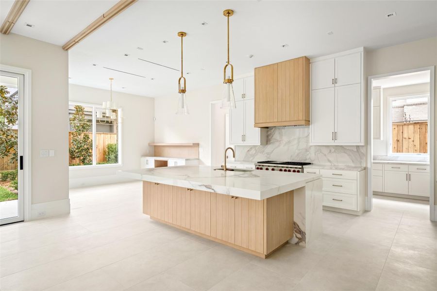 Warm wood detailing and sculptural lighting elevate the kitchen, while waterfall stone surfaces and abundant storage—within the island and throughout—add both beauty and function.