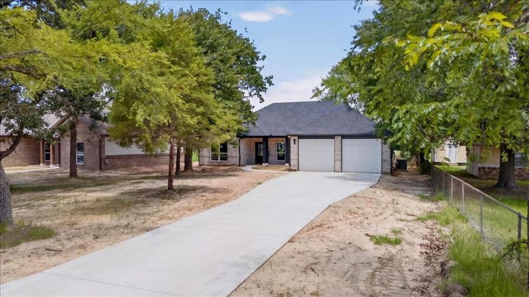Exterior featuring a durable dark shingle roof, two-car garage and a concrete driveway that provides parking for multiple cars.