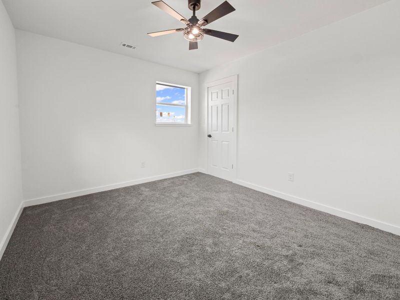 Neutral-toned carpeting paired with white walls, a single window, a panel door, and a ceiling fan with integrated lighting