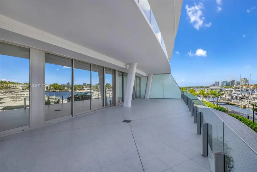 Expansive covered terrace featuring large-format tile flooring, floor-to-ceiling glass sliding doors, and a transparent glass railing system