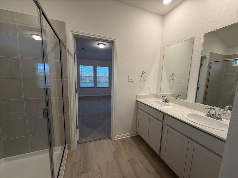 Full bath featuring a stall shower, double vanity, and light wood-type flooring Full bath featuring a stall shower, double vanity, and light wood-type flooring