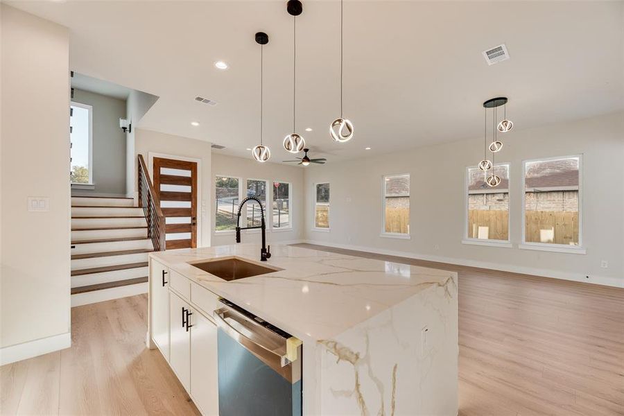 Kitchen featuring light stone counters, white cabinetry, decorative light fixtures, light wood-style flooring, and open floor plan Kitchen featuring light stone counters, white cabinetry, decorative light fixtures, light wood-style flooring, and open floor plan