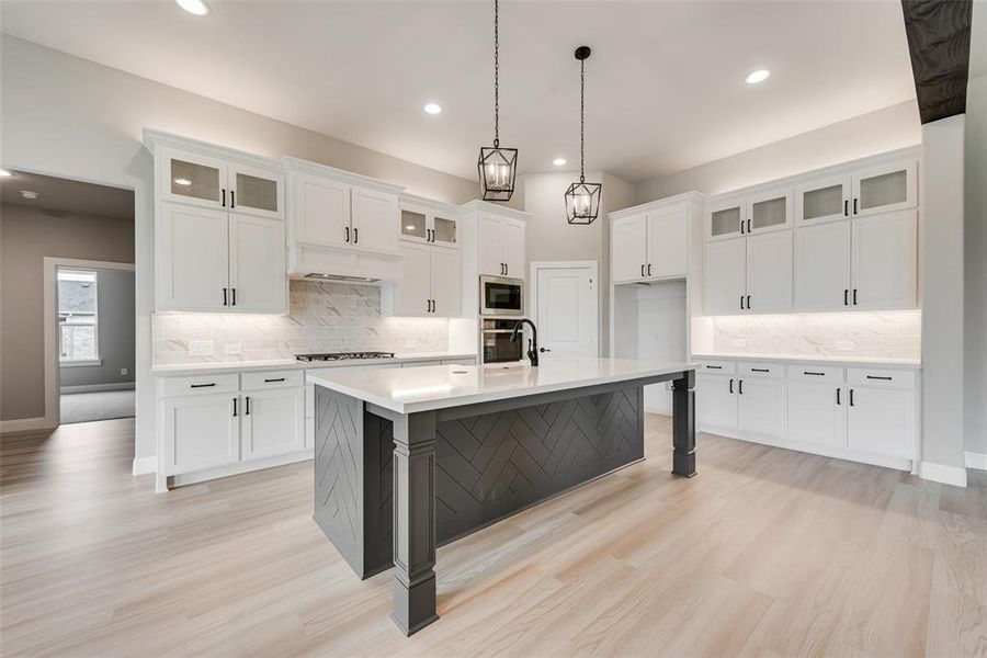 Kitchen featuring pendant lighting, light hardwood / wood-style floors, a kitchen island with sink, white cabinets, and appliances with stainless steel finishes