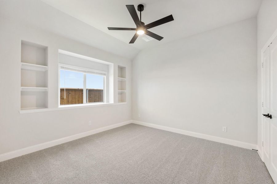 Empty bedroom with vaulted ceiling, black ceiling fan, built-in shelves, and carpet flooring Empty bedroom with vaulted ceiling, black ceiling fan, built-in shelves, and carpet flooring