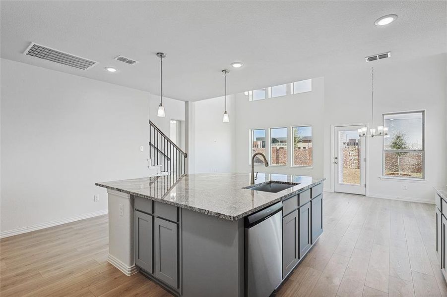 Kitchen with stainless steel dishwasher, light stone countertops, light wood finished floors, and a kitchen island with sink Kitchen with stainless steel dishwasher, light stone countertops, light wood finished floors, and a kitchen island with sink