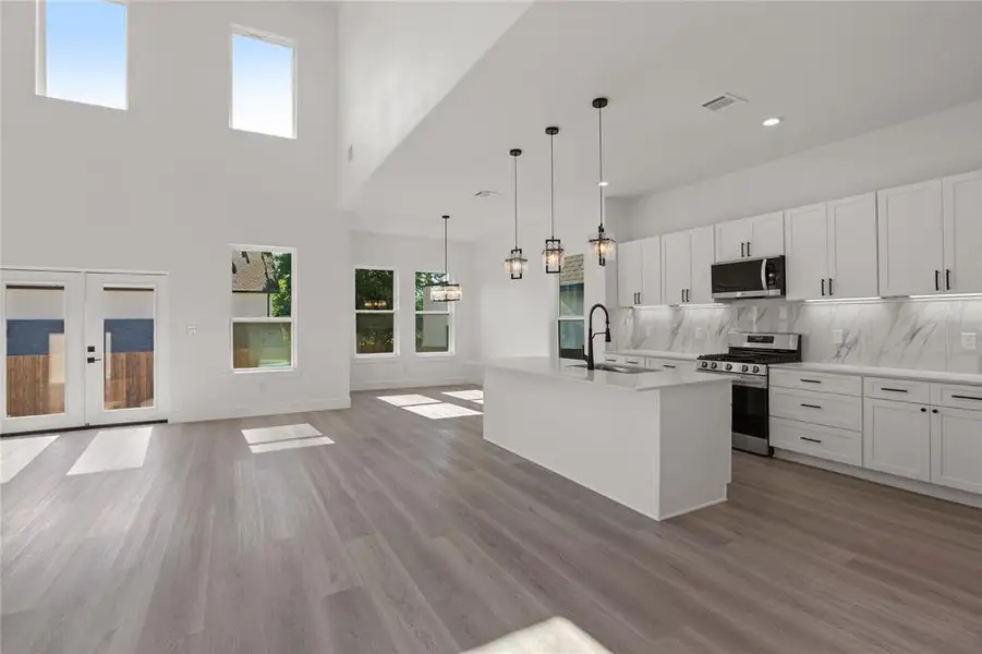 Kitchen featuring french doors, tasteful backsplash, appliances with stainless steel finishes, a center island with sink, and open floor plan