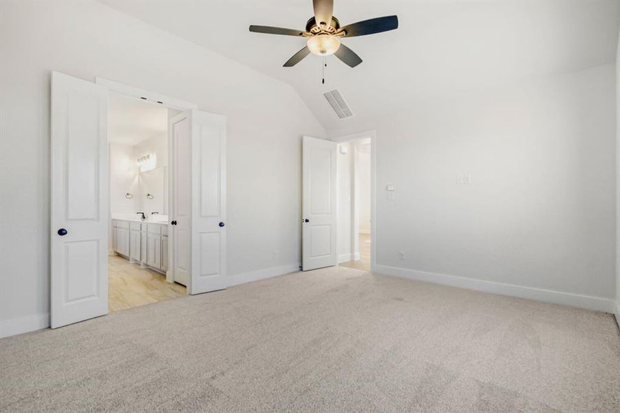 Unfurnished bedroom with light carpet, vaulted ceiling, a ceiling fan, and ensuite bathroom