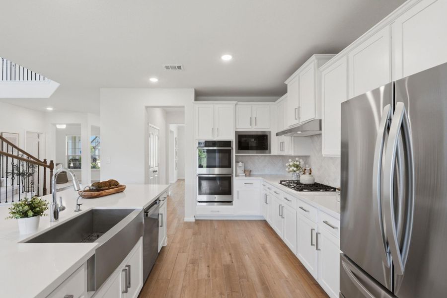 This spacious kitchen features modern stainless steel appliances, white cabinetry, and a large island with a farmhouse sink. The bright, open layout is complemented by wood flooring and recessed lighting, perfect for cooking and entertaining.