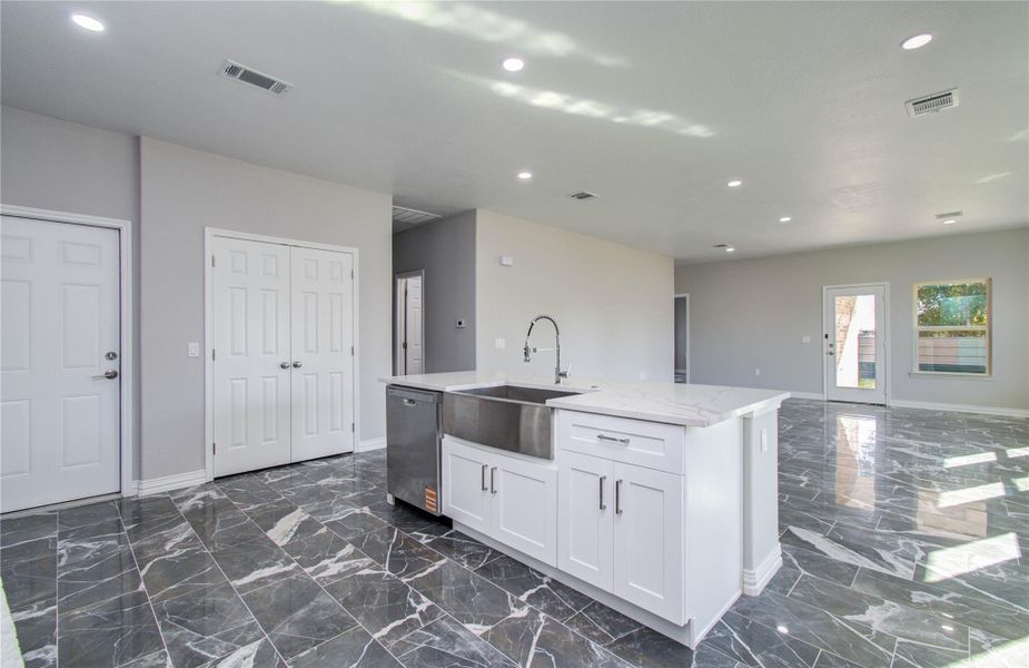 This spacious, modern open-concept kitchen features sleek marble flooring, a large island with a deep sink, and ample lighting. The neutral color palette enhances the bright, airy feel, complemented by a door and window leading to the outdoor space.