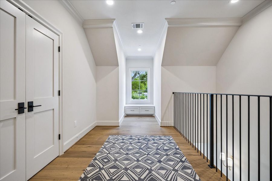 Light-filled upper-level landing featuring beautiful wide-plank French white oak flooring, enhanced by crown molding and lovely trim. A charming window seat offers a cozy nook framed by natural light, while the open railing adds architectural interest and overlooks the level below. Versatile in design, ideal for play area, reading or additional lounge area.
