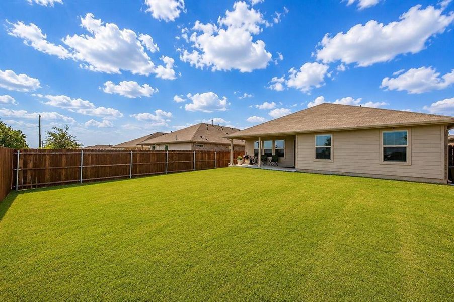 Expansive fenced backyard featuring a manicured lawn, a covered patio, and multiple windows