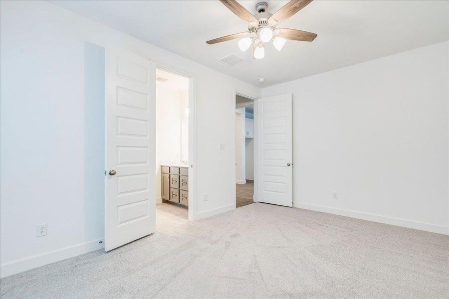 This room features light-colored carpeting, white walls, and a ceiling fan with a light fixture