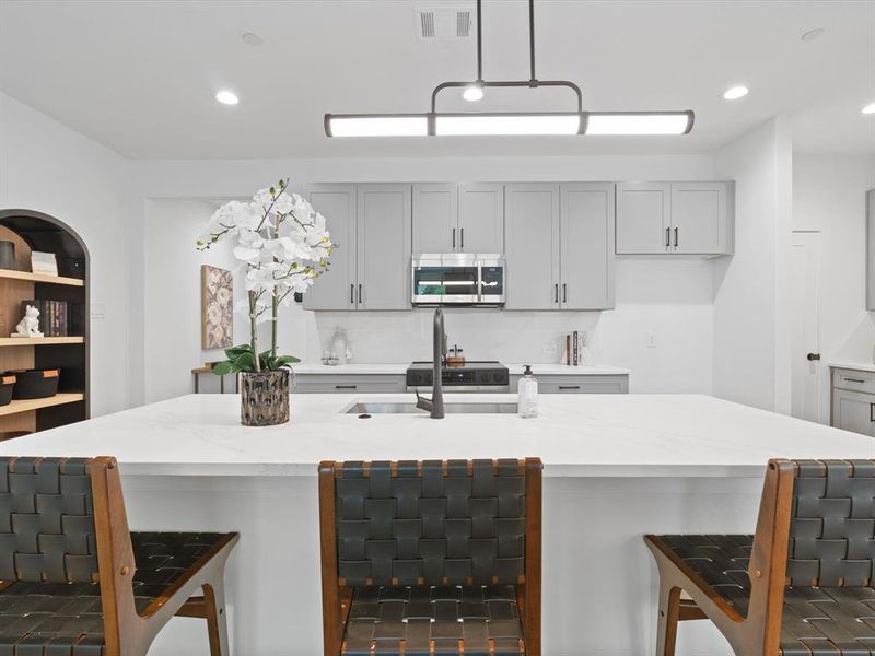 Kitchen featuring stainless steel microwave, visible vents, a breakfast bar, and light stone counters Kitchen featuring stainless steel microwave, visible vents, a breakfast bar, and light stone counters
