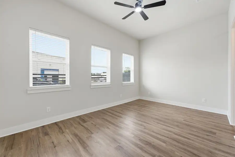 Bright and spacious bedroom featuring wide-plank wood-look flooring, abundant natural light from multiple windows, and a modern ceiling fan.