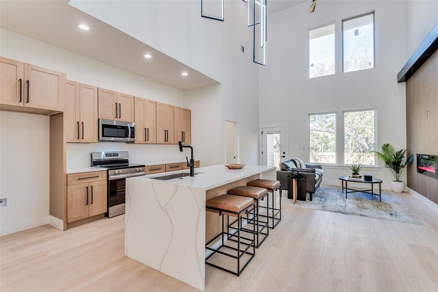 Kitchen with light wood finish cabinets, stainless steel appliances, light wood finished floors, a breakfast bar, and a high ceiling