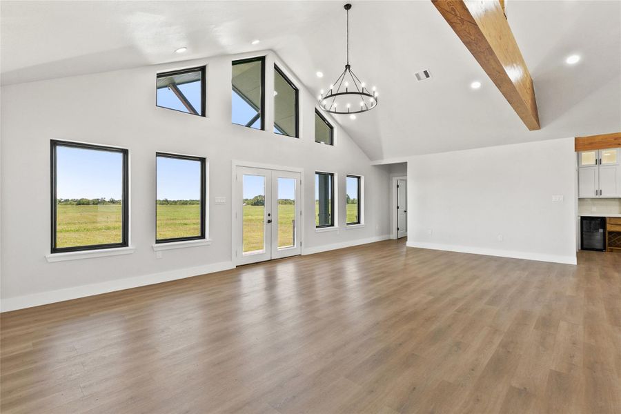 Large windows extending to the peak of the vaulted ceiling draw in abundant natural light and showcase the wide-open views beyond. French doors provide easy access to the backyard and outdoor living space.
