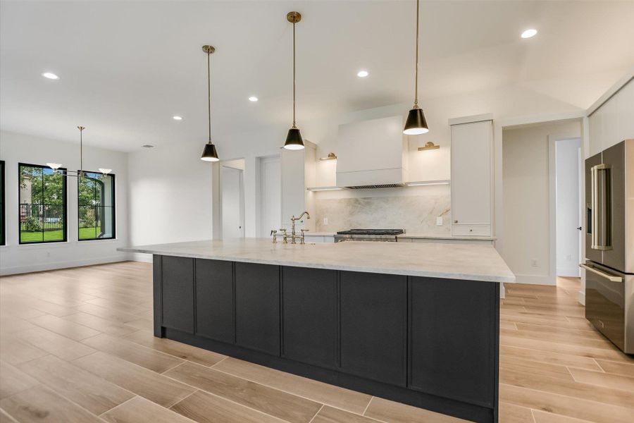 Open-concept kitchen featuring a large central island with a light-colored countertop, dark cabinetry, and three pendant lights