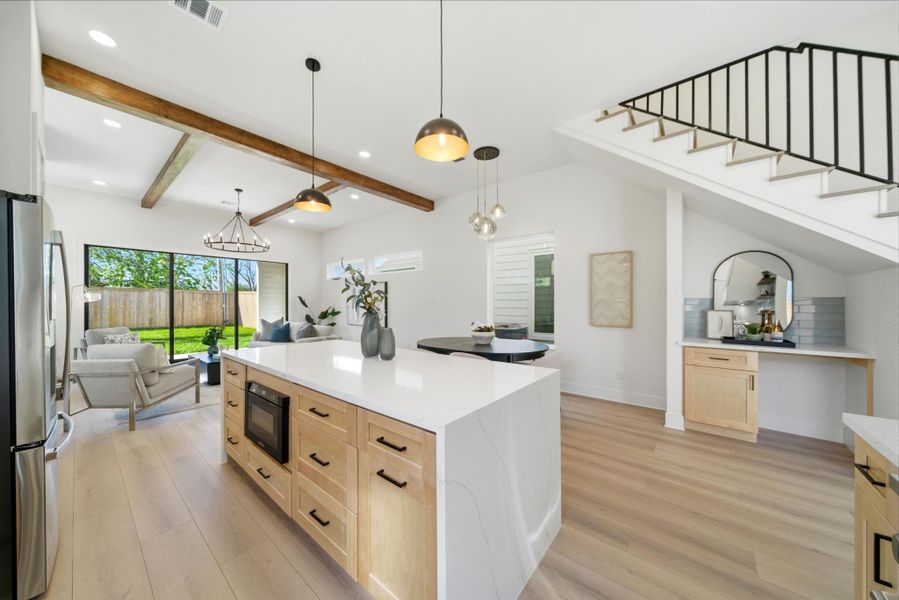 This photo showcases a modern, open-concept kitchen and living area with light LVP floors, a large island with ample storage, and stylish pendant lighting.