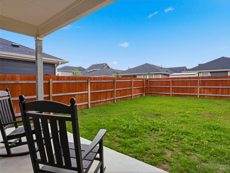 An enclosed grassy lawn stands framed by a tall wooden fence under clear blue skies. An enclosed grassy lawn stands framed by a tall wooden fence under clear blue skies.