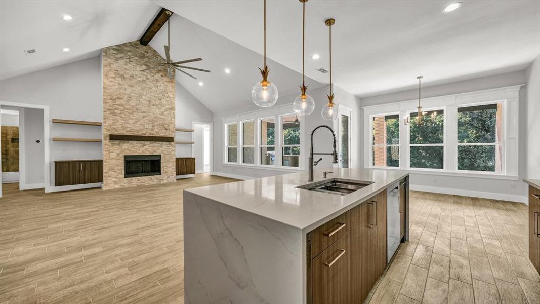 Kitchen with an island with sink, light wood-type flooring, stainless steel dishwasher, sink, and a fireplace