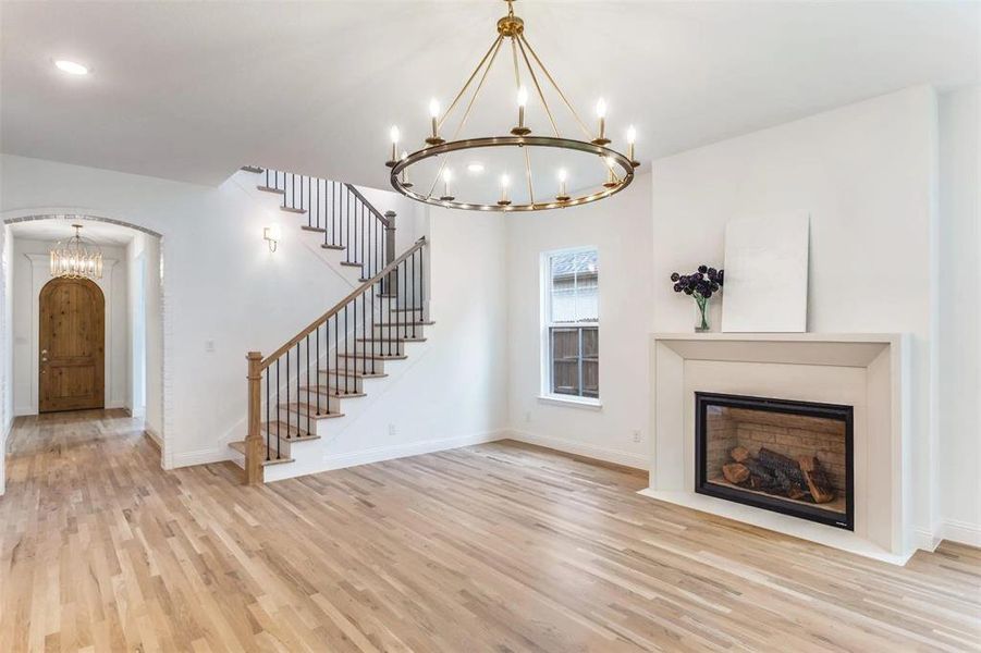 Unfurnished living room featuring a chandelier, light wood-type flooring, a fireplace, arched walkways, and stairway