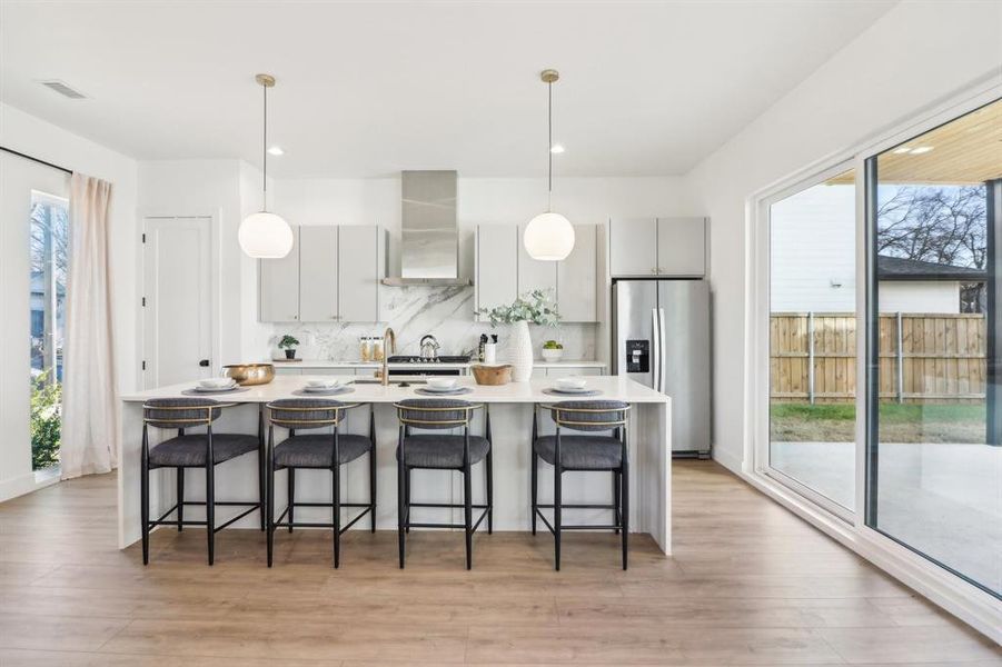 Kitchen featuring stainless steel fridge, tasteful backsplash, wall chimney range hood, light hardwood / wood-style floors, and a breakfast bar area